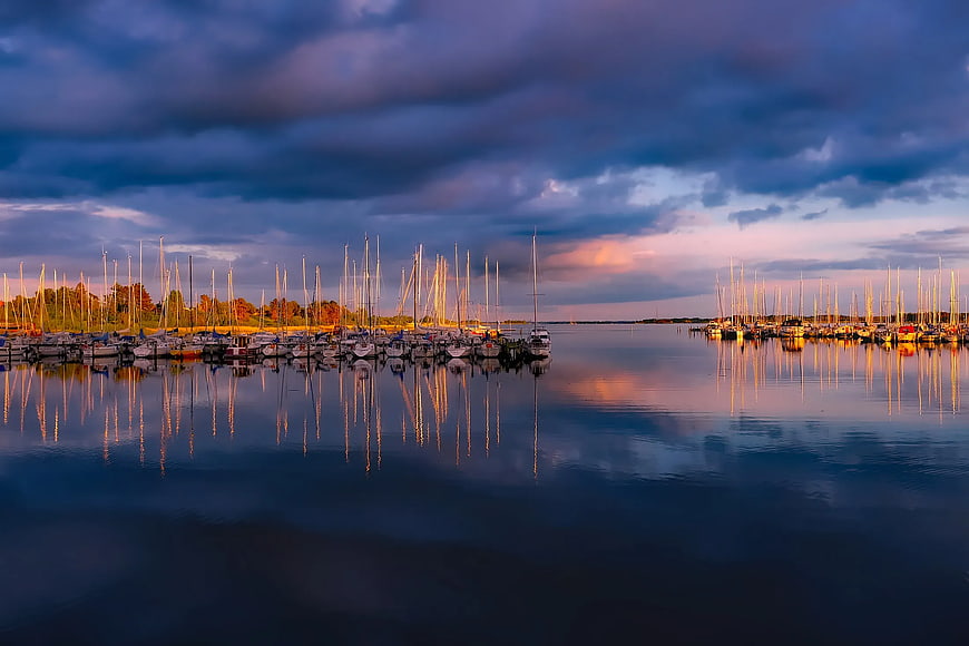 Serene marina at dusk with sailboats and dramatic sky reflections