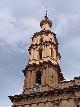 Low angle view of historic beige church bell tower against cloudy sky