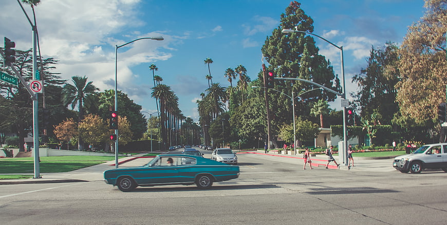Vintage teal car driving through sunny California street intersection