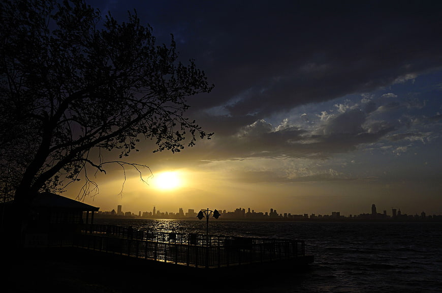 Dramatic Sunset Silhouette Over Lake With City Skyline