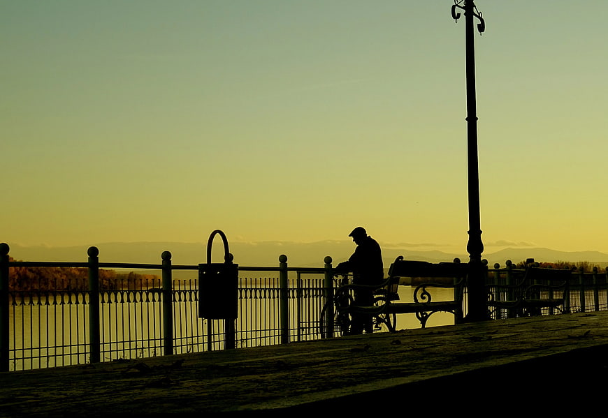 Silhouette of Man with Bicycle on Riverside Promenade at Sunset