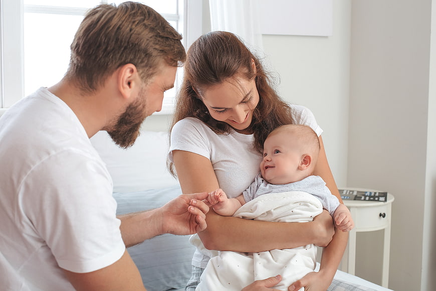 Happy Parents Holding Smiling Baby in Bedroom