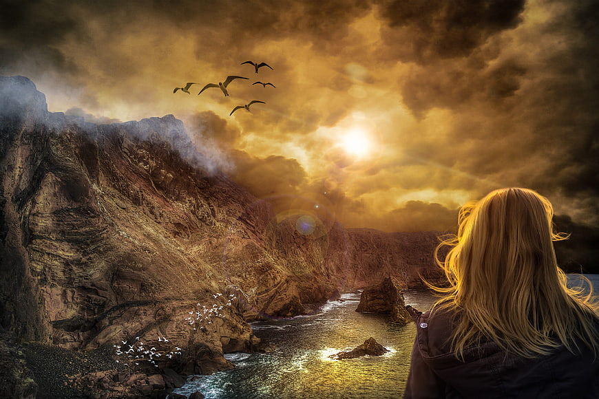 Woman Watching Dramatic Golden Sunset Over Rocky Coastline