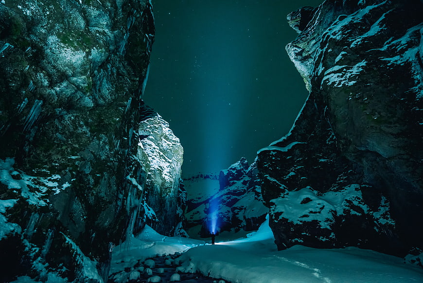 Lone Hiker with Flashlight in Snowy Mountain Canyon at Night