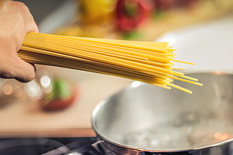 Hand holding uncooked spaghetti over boiling water pot