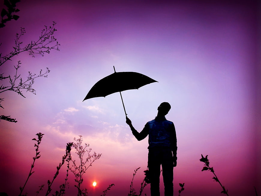 Silhouette of Man Holding Umbrella Against Purple Sunset Sky