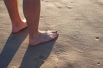 Barefoot man standing on sandy beach at sunset