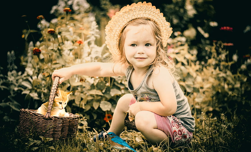 Little girl in straw hat with kitten in basket and blue bird in garden