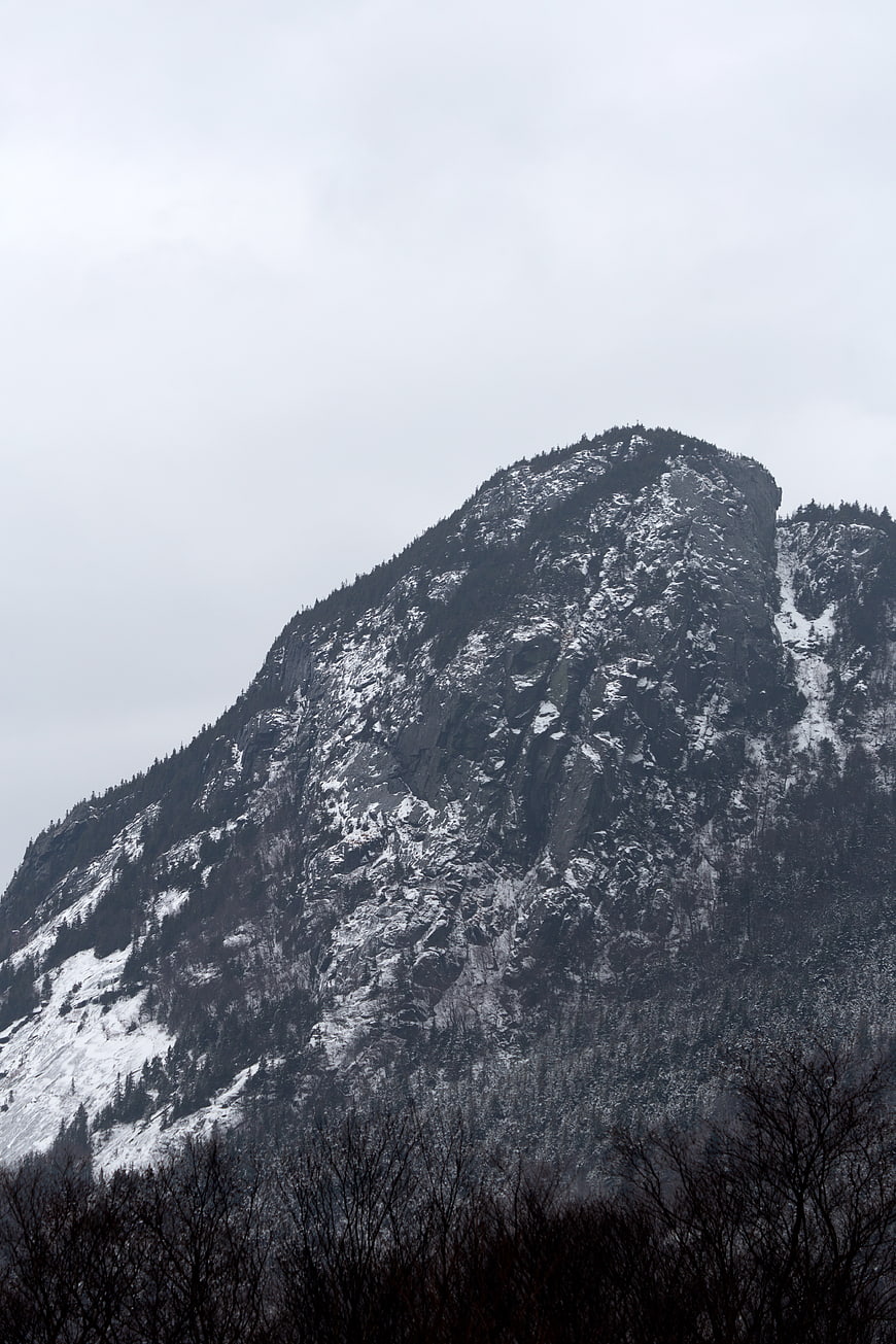 Snowy Mountain Peak with Dark Forest and Overcast Sky