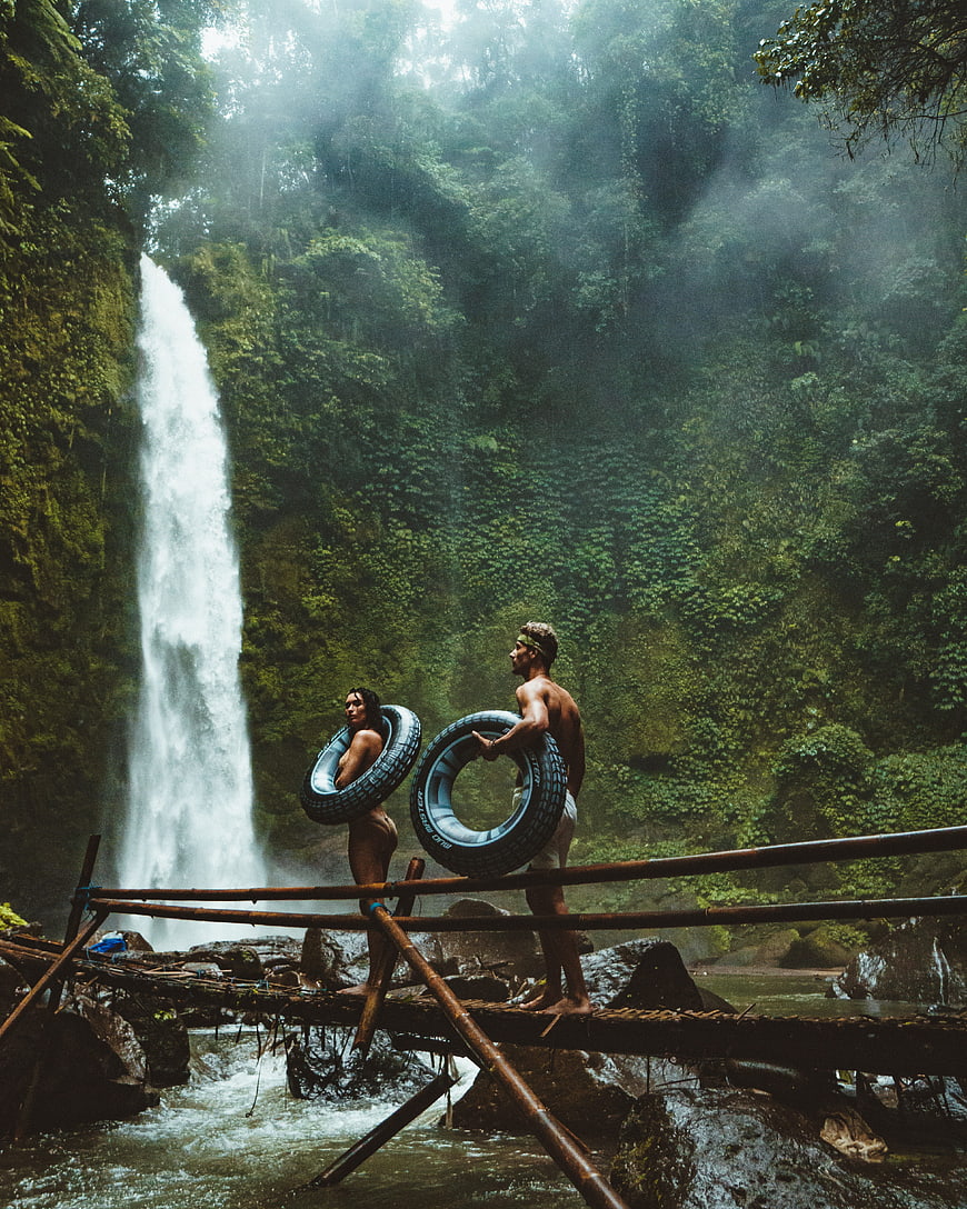 Couple with tires on bamboo bridge near tropical waterfall