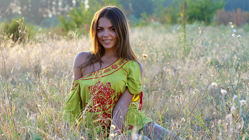 Smiling Woman in Green Dress Sitting in Grassy Field
