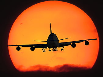Silhouette of a large airplane landing against a massive orange sunset