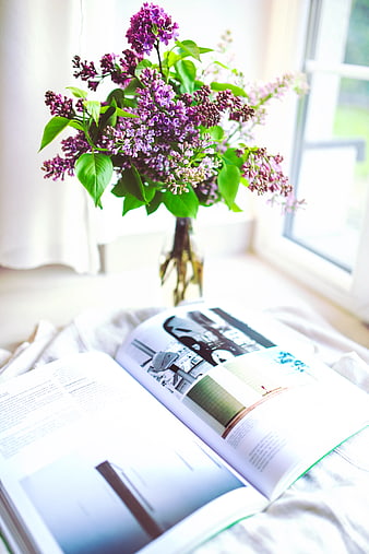 Purple lilac flowers in vase with open book on bed