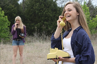 Young woman laughing with vintage yellow rotary phone outdoors