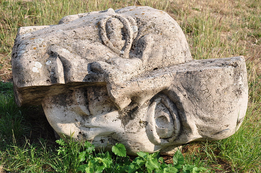 Ancient weathered stone head sculpture lying in grassy field