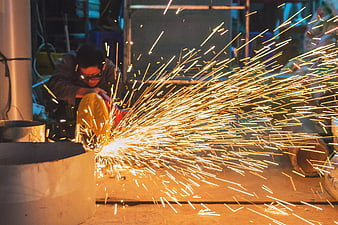 Industrial Worker Grinding Metal With Flying Sparks In Factory