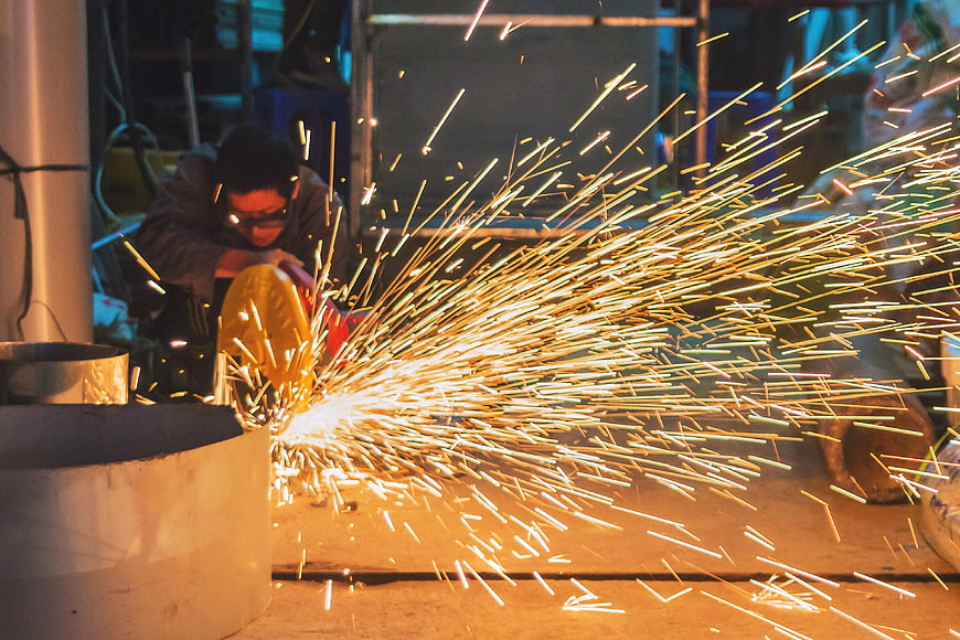 Industrial Worker Grinding Metal With Flying Sparks In Factory