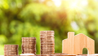 Wooden house model and stacked coins on green background