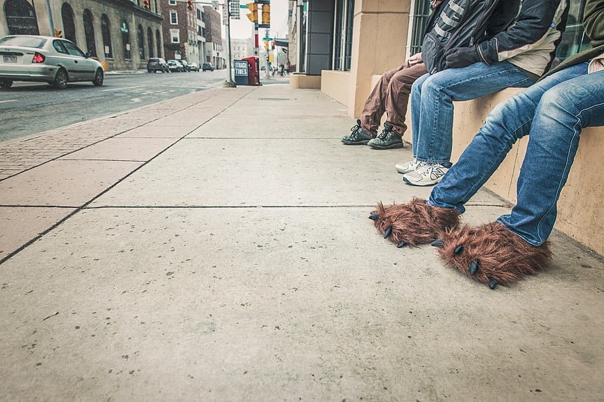 Person wearing furry monster shoes sitting on city sidewalk
