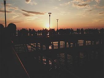 Silhouetted crowd on pier watching sunset over ocean