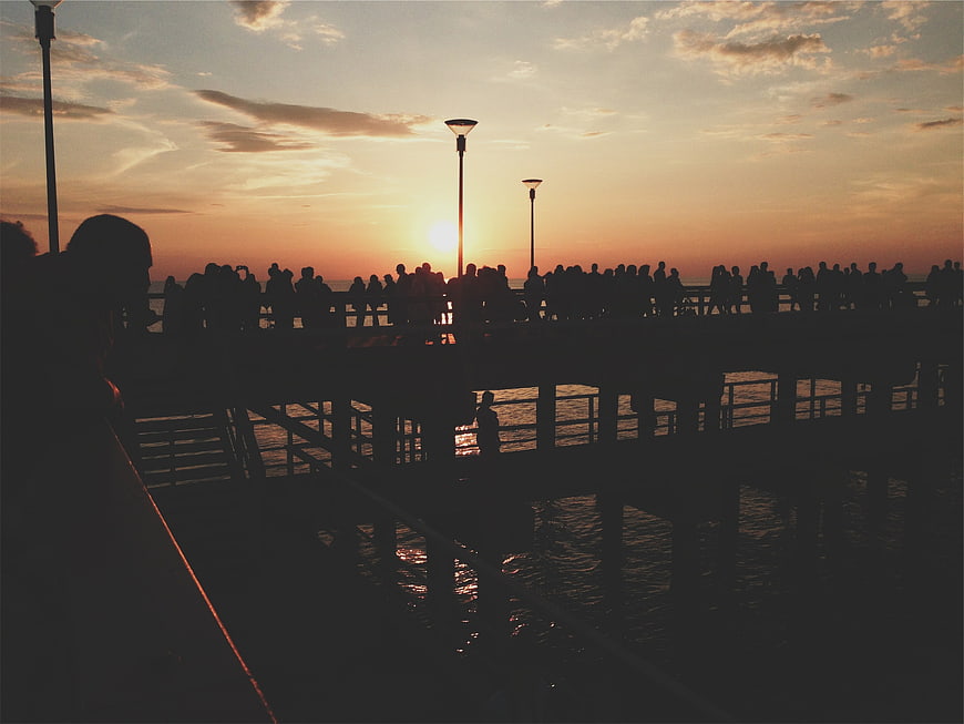 Silhouetted crowd on pier watching sunset over ocean
