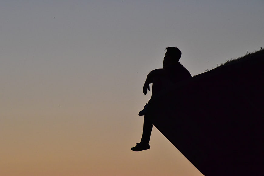 Silhouette of Man Sitting on Cliff Edge at Sunset