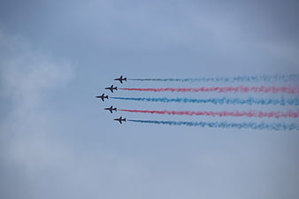 Five jets flying in formation with red and blue smoke trails