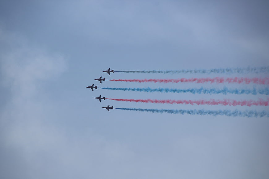 Five jets flying in formation with red and blue smoke trails