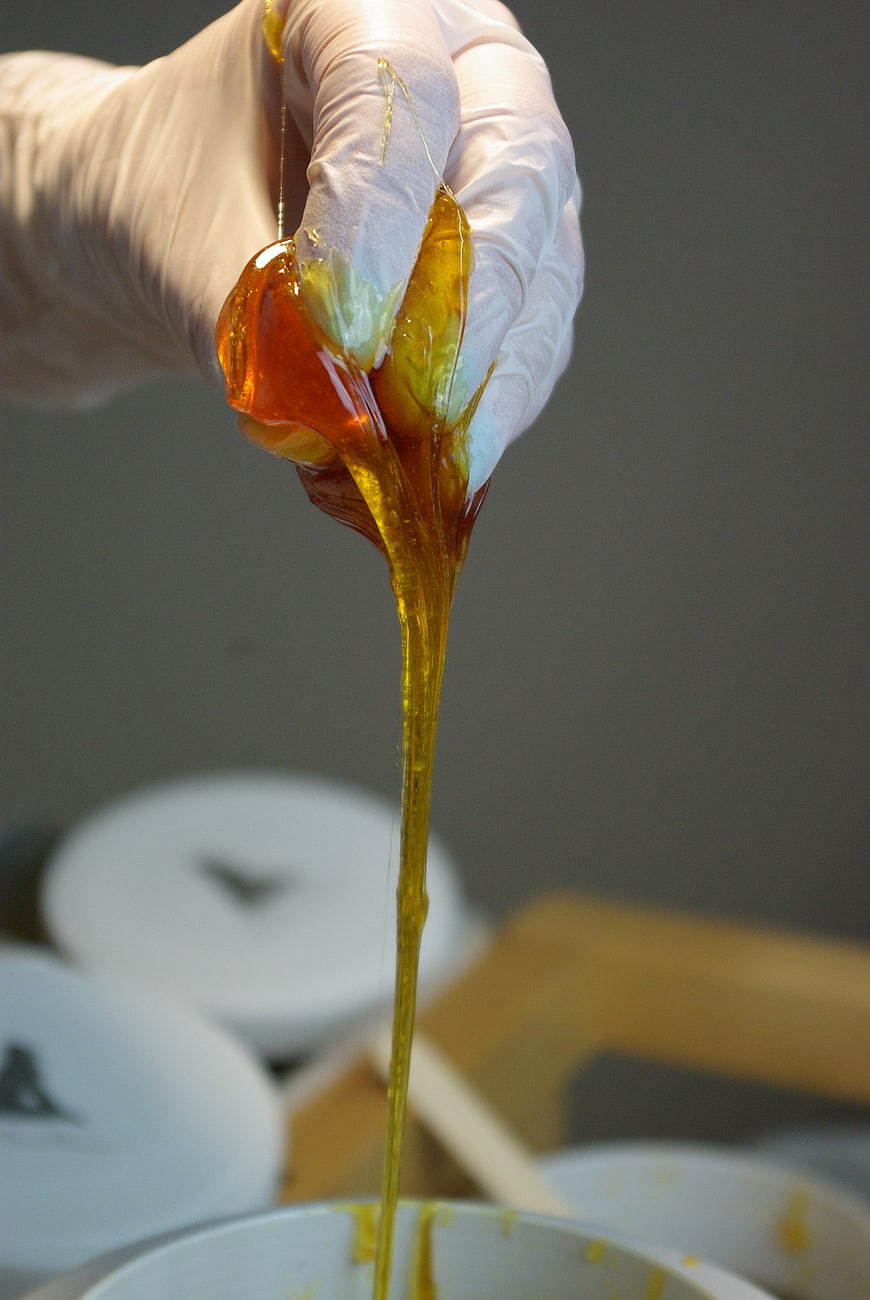Gloved hand squeezing amber hair removal wax