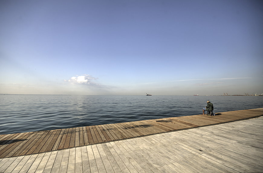 Lone Fisherman Sitting on Wooden Dock by Calm Sea