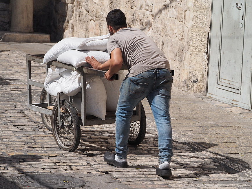 Man pushing heavy cart with sacks on cobblestone street