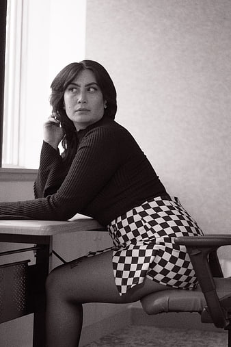 Woman in Checkered Skirt Sitting at Desk in Black and White