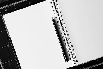 Black and white spiral notebook with pen on cutting mat
