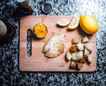 Overhead view of seasoned fish fillet with roasted potatoes and lemon on wooden board