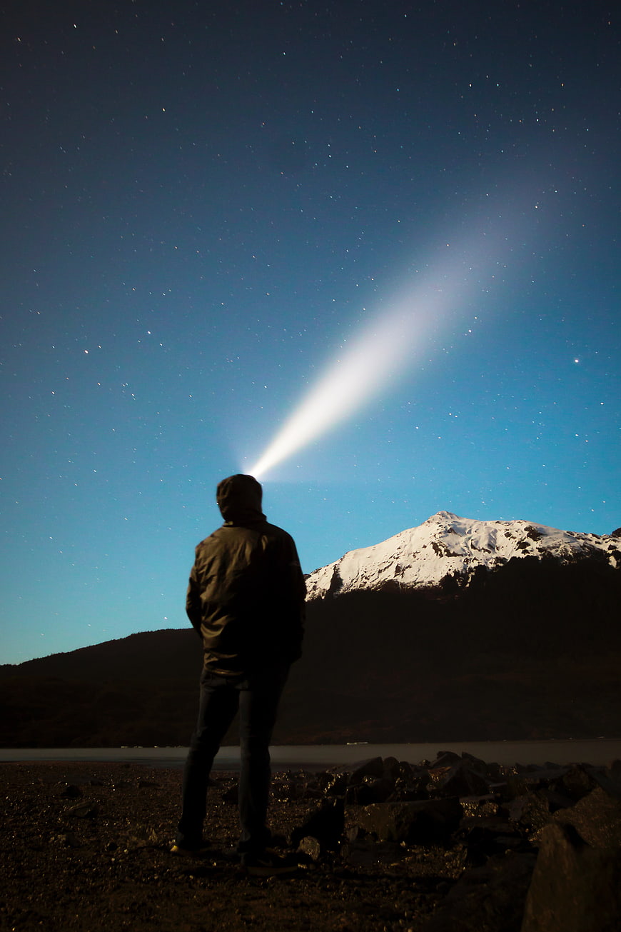 Man with Flashlight Beam in Starry Night Sky