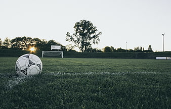 Football ball on grass field at sunset with goal in background