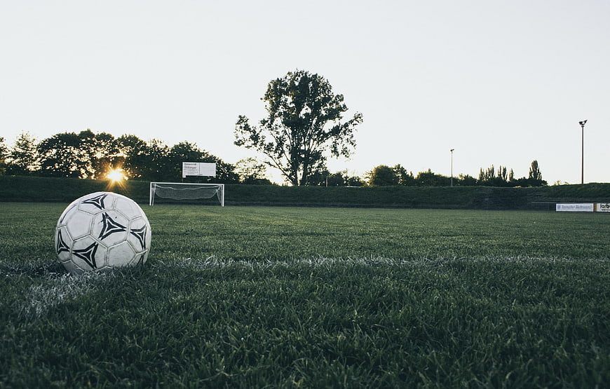 Football ball on grass field at sunset with goal in background