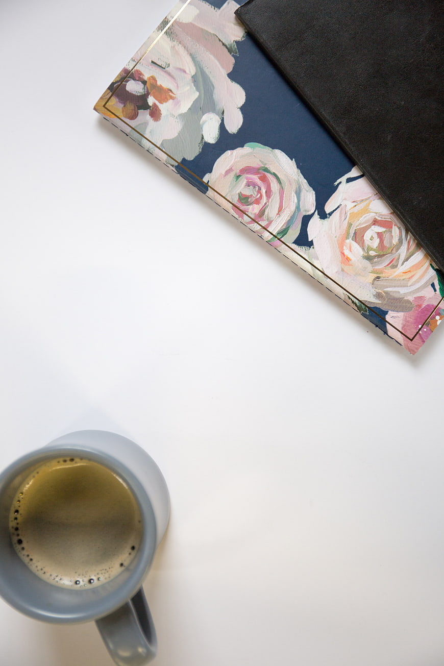 Minimalist flat lay of coffee cup and floral notebook on white background