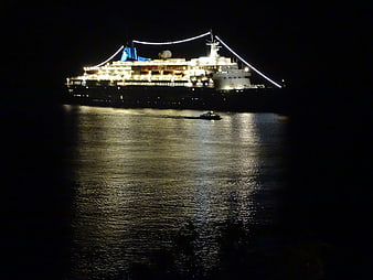 Illuminated cruise ship sailing on dark ocean at night