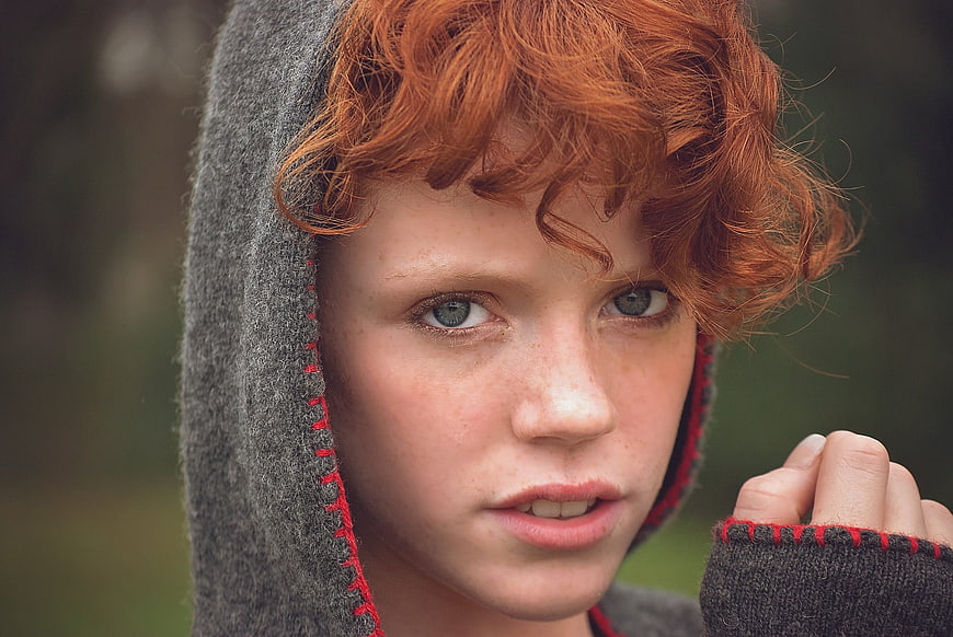 Portrait of young girl with red hair and blue eyes in grey hood