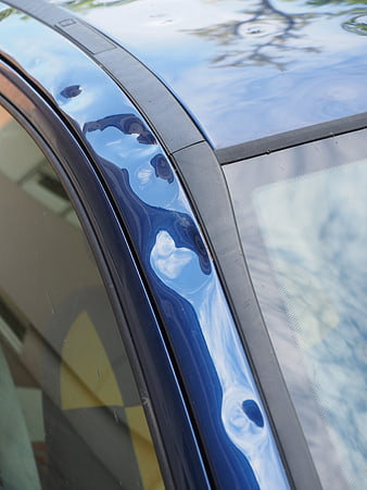 Close-up of blue car roof with visible hail damage and paint dents