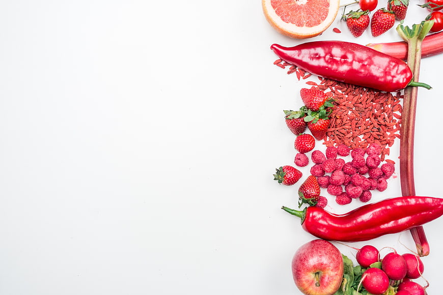 Flat lay of red fruits and vegetables on white background