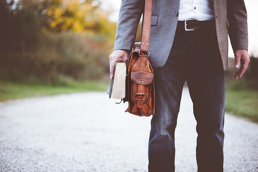 Man in Blazer Holding Bible and Leather Satchel on Path