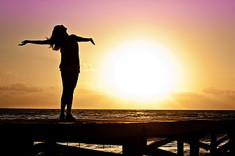 Silhouette of Woman with Arms Outstretched on Pier at Sunset