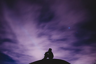 Silhouette of a man sitting on a hill under a purple night sky