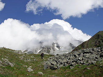 Hikers on rocky mountain trail with clouds and blue sky