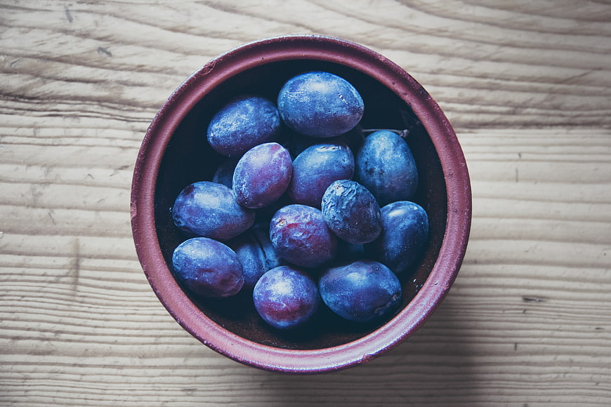 Top view of fresh plums in a rustic ceramic bowl on wood