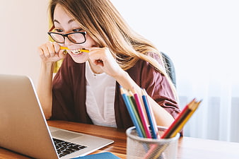 Stressed female student biting pencil while studying on laptop
