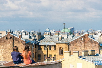 Two women sitting on a rooftop overlooking city buildings