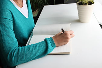 Woman Writing in Notebook on White Desk